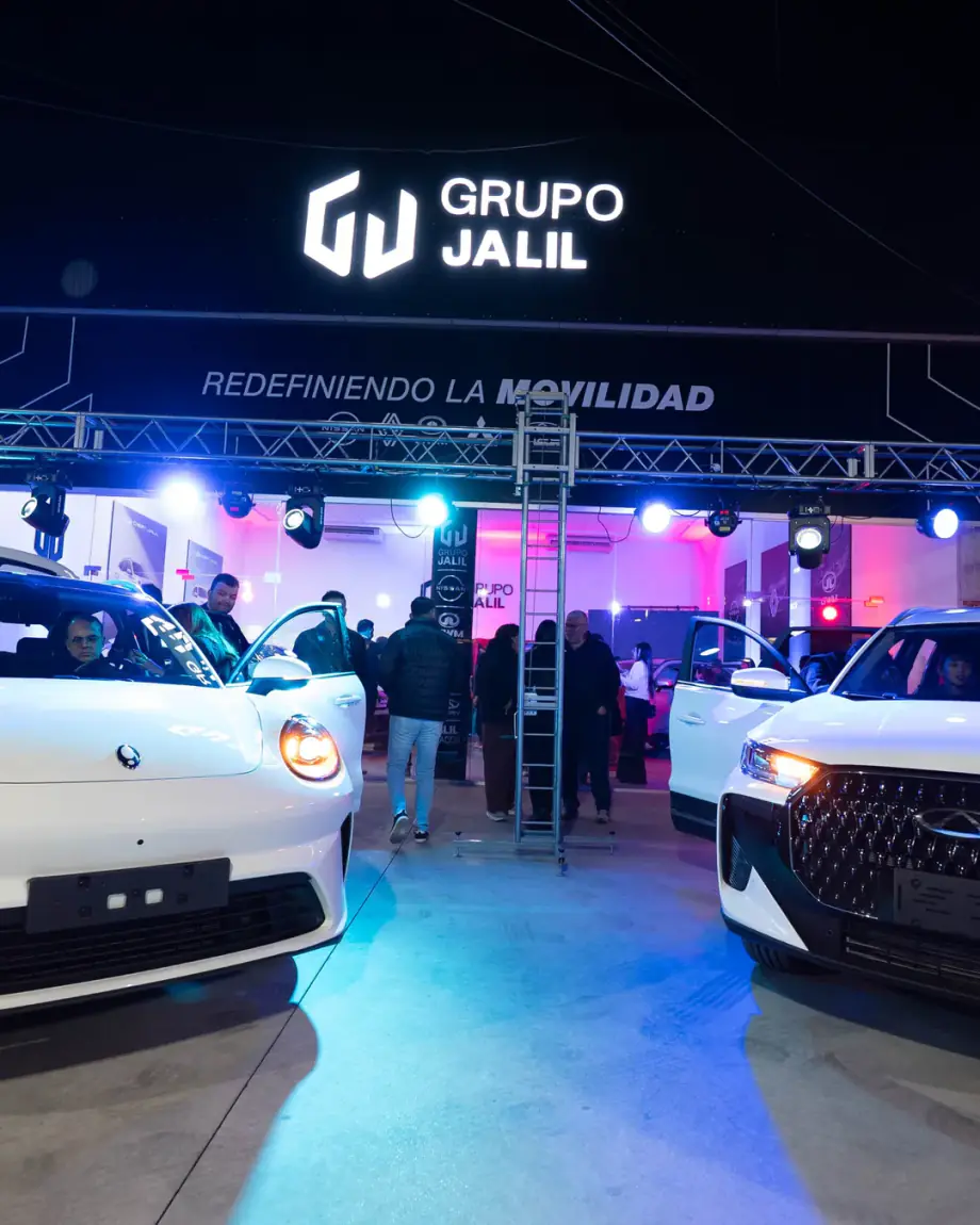 Dos autos en el stand de Grupo Jalil de noche, con el cartel y el lema Redefiniendo la movilidad